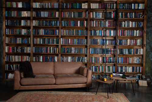 an inviting brown leather sofa welcomes you to nestle among a roomful of books organized on floor to ceiling dark wood bookcases.
